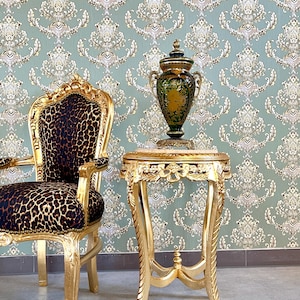 Può includere: Una lussuosa scena d'interni con una sedia dorata con rivestimento leopardato, un tavolino abbinato e un vaso decorativo. La sedia e il tavolo presentano intagli ornati. Lo sfondo è una carta da parati a motivi nei toni del verde e del bianco.