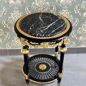 May include: A black and gold side table with a round, black marble top. The table has a lower shelf with a woven design and ornate gold accents. The legs are black with gold detailing, and the table has a classic, elegant style.