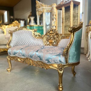 Può includere: Un divanetto in legno dipinto in oro con intricati dettagli floreali intagliati sulla struttura. La seduta e lo schienale sono rivestiti in tessuto damascato azzurro e beige, mentre i lati esterni sono in velluto azzurro a tinta unita.