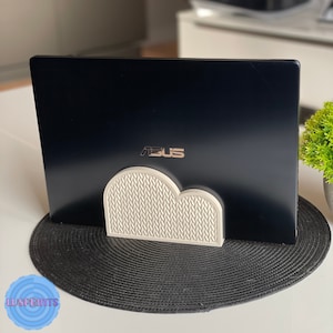 May include: A white cloud-shaped laptop stand with a textured surface. The stand is holding up a black laptop with the ASUS logo on the back.