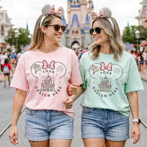 May include: Two women wearing matching t-shirts and headbands with mouse ears. The shirts are light pink and mint green, featuring a castle design with the text "YOUR DESIGN HERE". They are wearing denim shorts and sunglasses, walking in front of a castle.