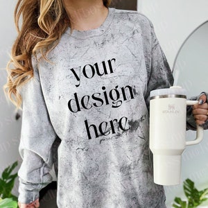 Może przedstawiać: Szara bluza z przetarciami z napisem "your design here" w kolorze czarnym. Modelka nosi niebieskie dżinsy i trzyma biały kubek podróżny Stanley.