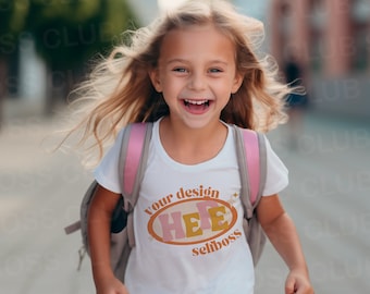 May include: A young girl wearing a white t-shirt with a pink and orange graphic that says "your design here selfboss". She is wearing a pink backpack and has a big smile on her face.