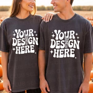 May include: Two charcoal gray t-shirts with the text "YOUR DESIGN HERE" in white, featuring a hand gesture graphic. The shirts are worn by a couple standing in a pumpkin patch.