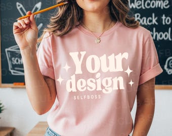 May include: A light pink t-shirt with the words "Your design" in a cream-colored, retro font, with starburst accents. The word "SELFBOSS" is below the design. The shirt has rolled-up sleeves and is being worn by a person.