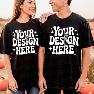Könnte beinhalten: Schwarze T-Shirts mit kurzen Ärmeln und dem weißen Text "YOUR DESIGN HERE", mit einer Handgeste. Die Shirts werden von zwei Personen auf einem Feld mit Kürbissen getragen.