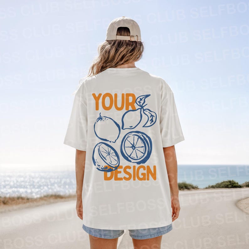 Puede incluir: Camiseta blanca con un dise&ntilde;o de c&iacute;tricos en azul y naranja. El texto "YOUR DESIGN" est&aacute; impreso en la parte posterior de la camiseta. La persona lleva una gorra de b&eacute;isbol beige y pantalones cortos vaqueros.