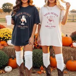 May include: Two oversized t-shirts, one dark grey and one cream, featuring a cocktail-themed graphic and the text "YOUR DESIGN" and "Selfboss Mockup". The shirts are paired with white leg warmers and cowboy boots. Pumpkins and hay bales are in the background.