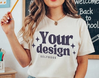 May include: Cream-colored t-shirt with the text "Your design" in a dark blue, stylized font, with the word "SELFBOSS" below. The shirt is short-sleeved and worn by a person. A pencil is held in the person's hand.
