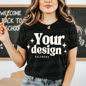 May include: Black t-shirt with the words "Your design" in a retro font, accented with starbursts. The word "SELFBOSS" is below the design. A pencil is held in the hand. The background includes a chalkboard with "WELCOME BACK TO SCHOOL" written on it.