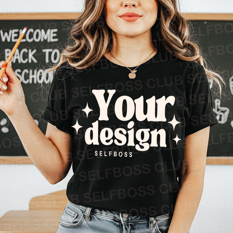 May include: Black t-shirt with the words "Your design" in a retro font, accented with starbursts. The word "SELFBOSS" is below the design. A pencil is held in the hand. The background includes a chalkboard with "WELCOME BACK TO SCHOOL" written on it.