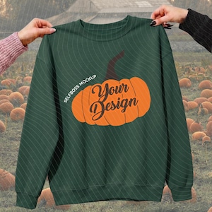 May include: A dark green crewneck sweatshirt featuring a large orange pumpkin graphic centered on the chest. The pumpkin design includes the black text "Your Design" in a cursive font and the smaller white text "SELFBOSS MOCKUP" above it.