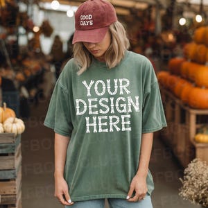 May include: A person wearing a green t-shirt with the text "YOUR DESIGN HERE" in white. The person is also wearing a maroon baseball cap with the words "GOOD DAYS" on it. The background includes pumpkins and gourds.