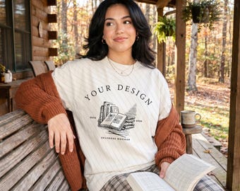 May include: A cream-colored t-shirt featuring a black line-art graphic of a stack of books and an open book. The text reads "YOUR DESIGN" in an arch above the books, with "ESTD 2020" on the sides and "SELFBOSS MOCKUP" printed below the books.