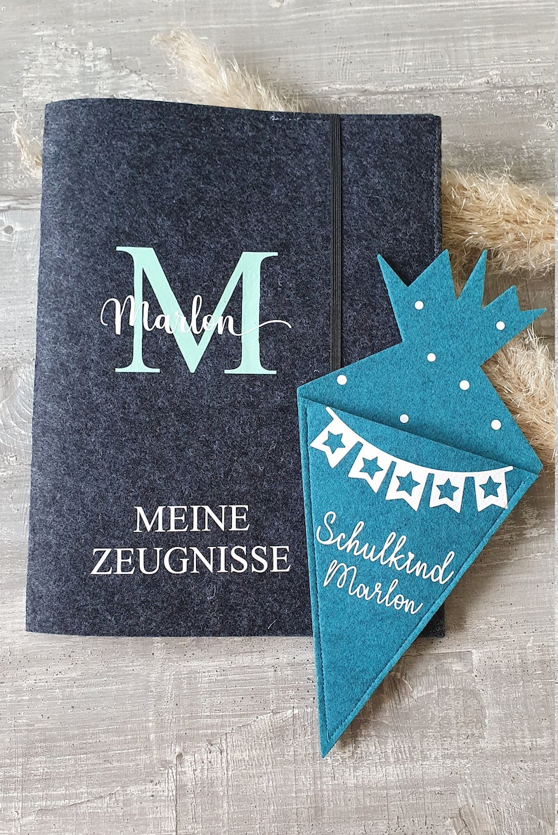 Puede incluir: Una carpeta de fieltro gris con el texto "Meine Zeugnisse" y una gran "M" verde con el nombre "Marlon" debajo. Un cono de fieltro turquesa con estrellas blancas y el texto "Schulkind Marlon" est&aacute; al lado de la carpeta.