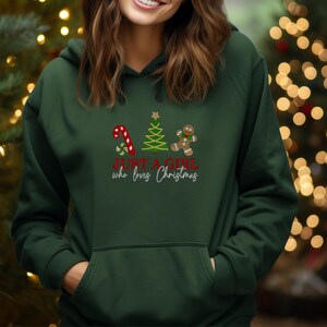 May include: Dark green hoodie featuring a candy cane, Christmas tree, and gingerbread man graphic. The text reads "JUST A GIRL who loves Christmas" in red and white.