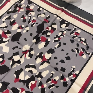 May include: A gray silk scarf with a leopard print pattern. The scarf has a white, burgundy, and gray border.