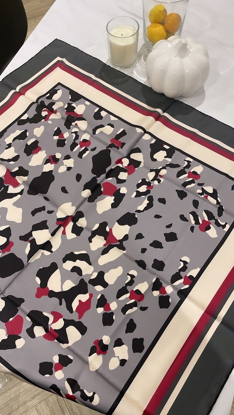 May include: A gray silk scarf with a leopard print pattern. The scarf has a white, burgundy, and gray border.