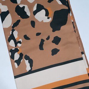 May include: A brown, black, and white patterned silk scarf with orange stripes at the bottom.