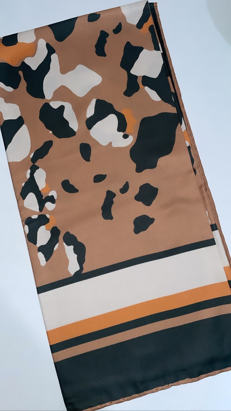 May include: A brown, black, and white patterned silk scarf with orange stripes at the bottom.
