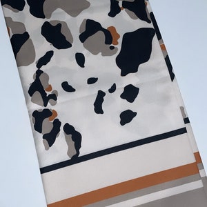 May include: A white scarf with a black, brown, and orange leopard print pattern. The scarf has a black border and a brown and white striped border.