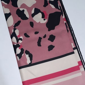 May include: A pink and black patterned scarf with a white and pink striped border. The scarf has a black trim around the edges.