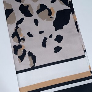 May include: A beige and black patterned scarf with a white and brown stripe border.