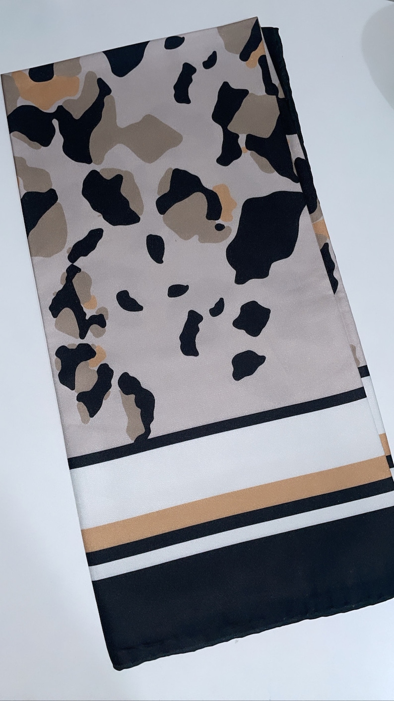 May include: A beige and black patterned scarf with a white and brown stripe border.