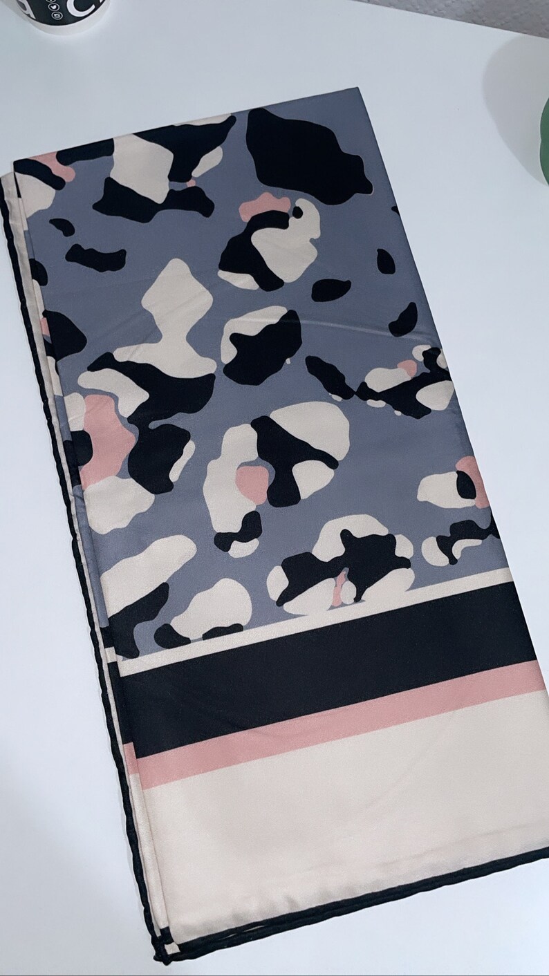 May include: A gray, black, and pink patterned scarf with a black and white striped border.