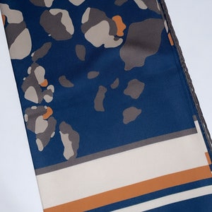 May include: A blue and white patterned scarf with orange accents. The scarf has a geometric design with a border of small brown circles.