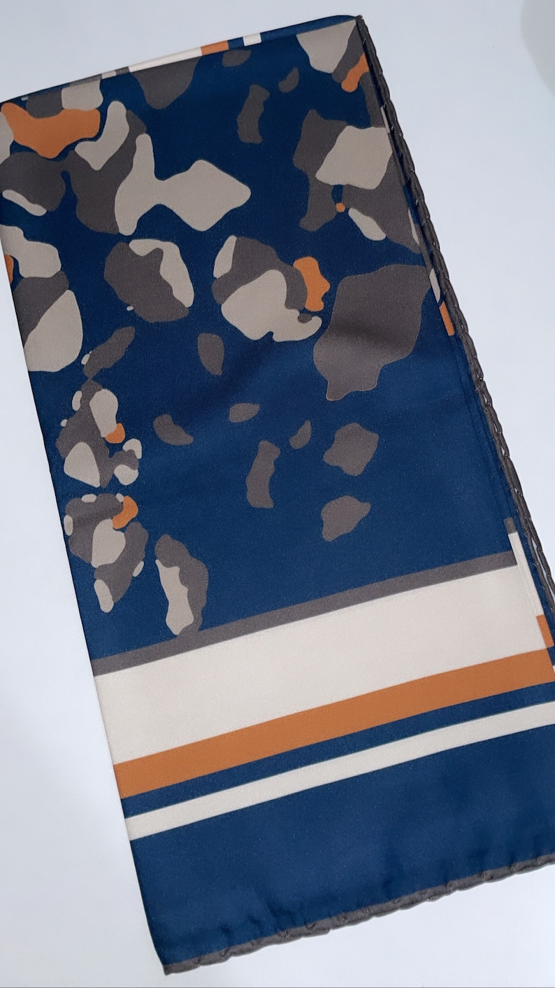 May include: A blue and white patterned scarf with orange accents. The scarf has a geometric design with a border of small brown circles.