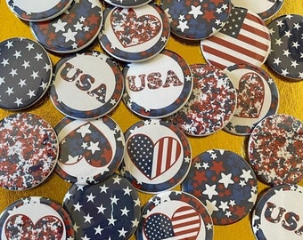 May include: A collection of patriotic pinback buttons with red, white, and blue designs. Some buttons feature the word "USA", while others display stars, hearts, and the American flag. The buttons are round and have a glossy finish.