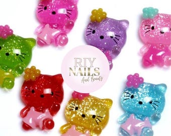 May include: Set of 7 colourful glitter cat charms with pink, purple, green, red, blue, and yellow glitter. Each charm has a flower on top and a pink dress. The charms are perfect for nail art, scrapbooking, and other crafts.