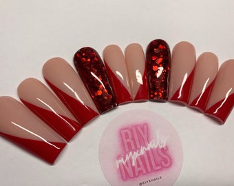 May include: Set of ten long, almond-shaped false nails with a red and nude design. The nails have a diagonal line separating the red and nude colors. One nail has red glitter.
