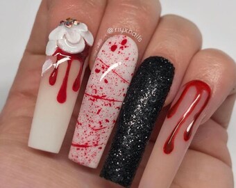 May include: Long, white, and nude fake nails with red blood dripping down them. One nail has a white 3D flower with red blood dripping down it. Another nail has black glitter. The nails are decorated with a Halloween theme.