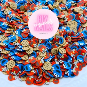 Puede incluir: Una imagen de primer plano de un montón grande de abalorios para uñas en forma de Cookie Monster y galletas, de colores vivos. Los abalorios están hechos de arcilla polimérica y son perfectos para añadir un toque divertido y caprichoso a tus uñas.