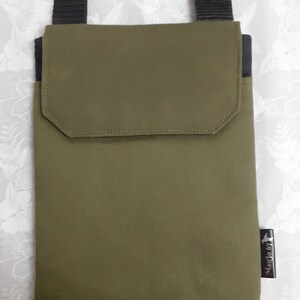 May include: A green canvas crossbody bag with a black strap and a black pocket on the front. The bag has a small black label with the text "Madjo 67" on the bottom right corner.