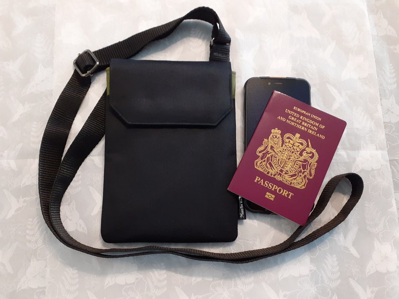 May include: A black crossbody bag with a zippered pocket and a green accent. The bag is lying on a white surface with a passport and a cell phone inside.