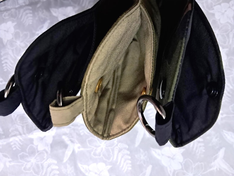 May include: Close-up of three small, open pouches in black, olive green, and tan. Each pouch has a metal ring and a snap closure. The pouches are made of a sturdy fabric and appear to be part of a larger bag or accessory.