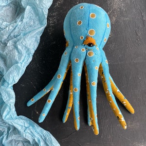 May include: A blue and yellow octopus plush toy with white polka dots. The octopus has eight tentacles and a large, round head with a single eye.