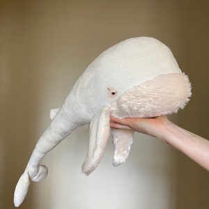 Puede incluir: Un juguete de peluche de ballena blanca con una textura suave y esponjosa. La ballena tiene una barriga ligeramente rosada y un peque&ntilde;o ojo bordado.