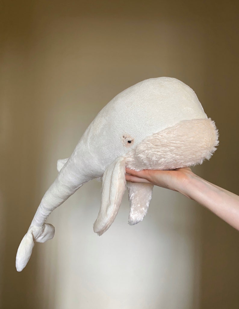 Puede incluir: Un juguete de peluche de ballena blanca con una textura suave y esponjosa. La ballena tiene una barriga ligeramente rosada y un peque&ntilde;o ojo bordado.
