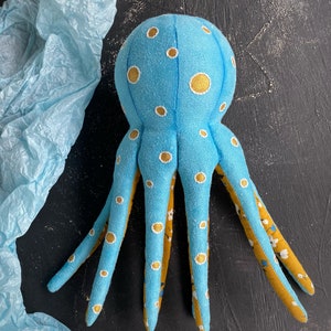 May include: A blue plush octopus with yellow and white polka dots. The octopus has eight tentacles and is made of soft fabric.