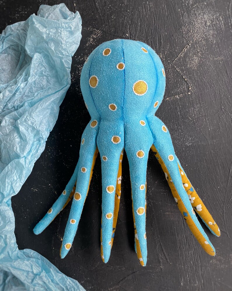 May include: A blue plush octopus with yellow and white polka dots. The octopus has eight tentacles and is made of soft fabric.