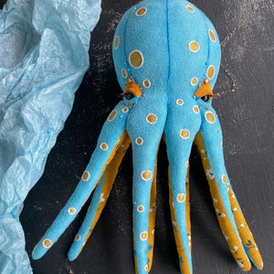 May include: A blue and yellow octopus plush toy with white polka dots. The octopus has eight tentacles and large, round eyes.