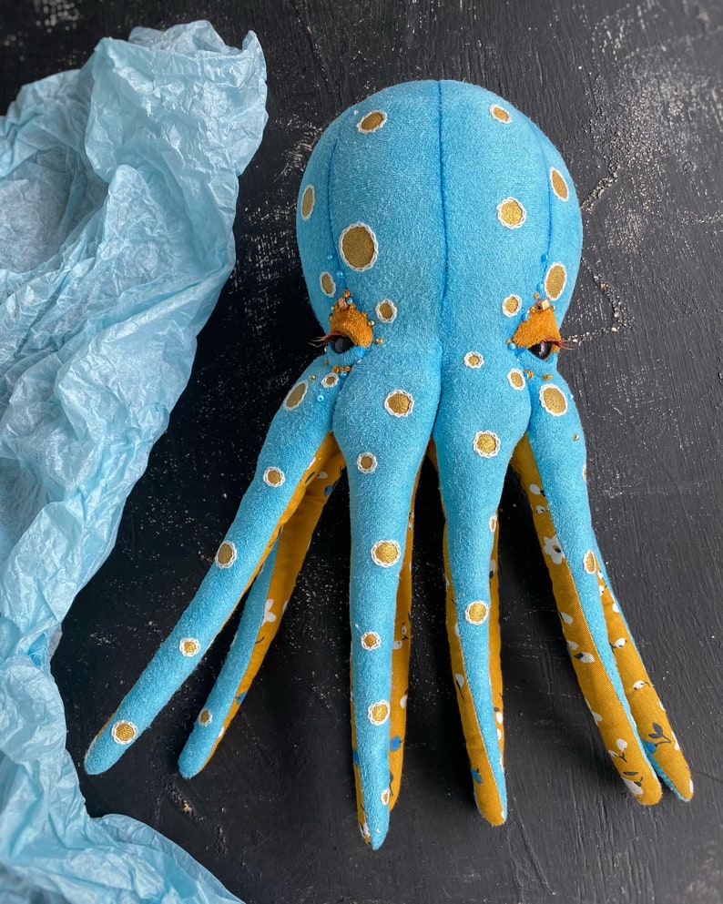 May include: A blue and yellow octopus plush toy with white polka dots. The octopus has eight tentacles and large, round eyes.