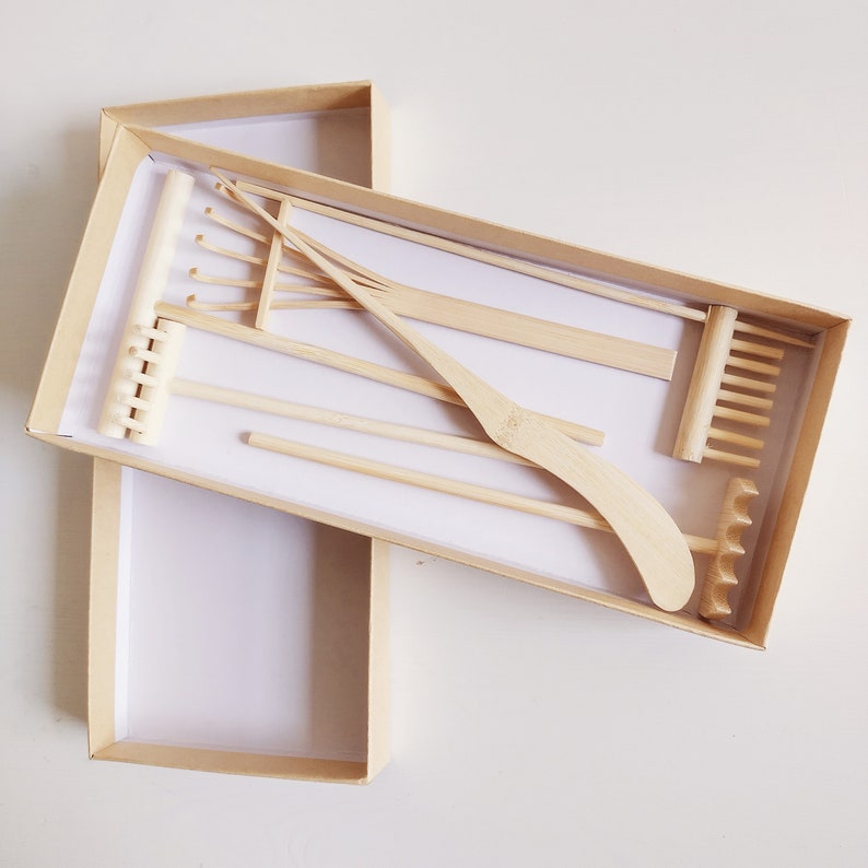 May include: A set of miniature wooden gardening tools in a brown cardboard box. The tools include a rake, a trowel, a cultivator, and a hand rake.