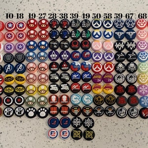 Peut inclure: Un ensemble de 76 capuchons ronds colorés pour joystick de manette de jeu, représentant divers logos et personnages de jeux vidéo, notamment Spider-Man, Mario, Overwatch et Call of Duty. Les capuchons sont disposés en rangées et numérotés de 1 à 76.