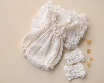 May include: White cotton baby romper with ruffled trim and matching leg warmers. The romper has a gathered skirt and a ruffled neckline.