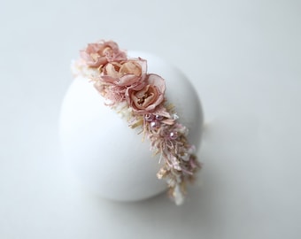 May include: A delicate headband with pink fabric flowers and gold accents. The headband is adorned with small white and pink beads.
